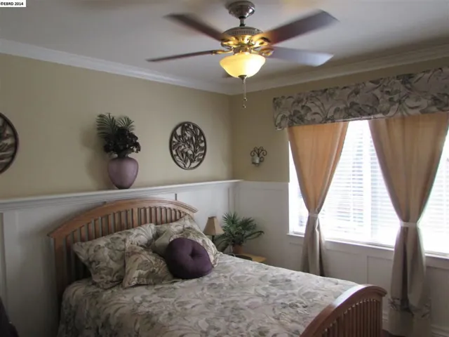 Large room has custom wainscoting, crown molding, shelf, ceiling fan and beautiful wood flooring.