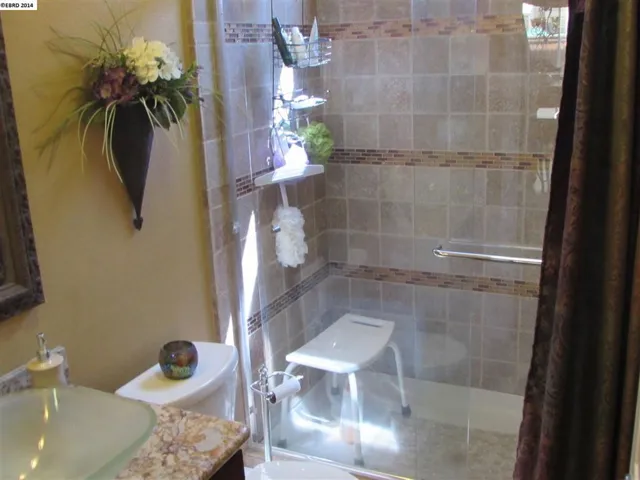 Shows the seamless glass shower door, custom stone work in shower, partial view of the vessel sink