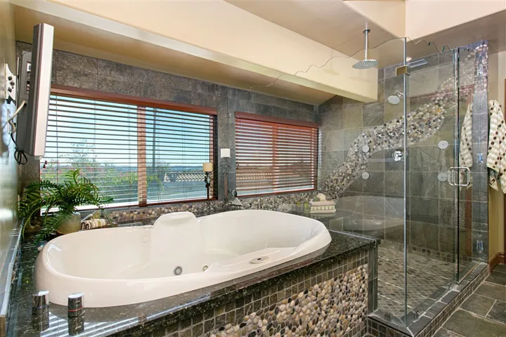 Jetted spa with wall mounted TV for the ultimate in relaxation. Custom cut frameless glass shower with top edge reflective of ocean waves.