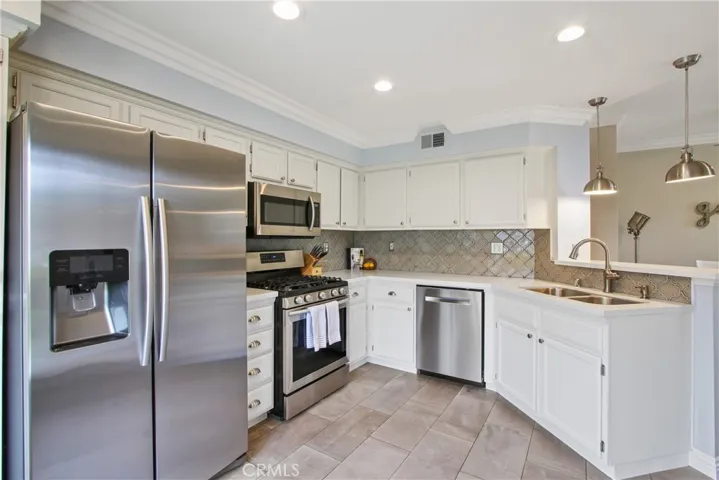 Designer tile backsplash, gorgeous quartz countertops and large neutral floor tiles are the foundation of this kitchen. A handsome stainless steel sink & appliances plus stainless steel accents on the cabinets & electrical outlets are the finishing details!