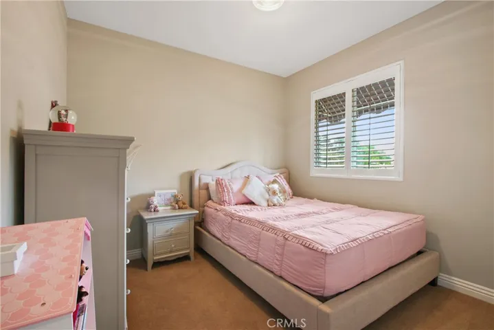 One of the secondary bedrooms featuring neutral paint and plantation shutters.
