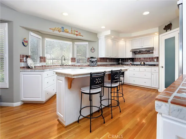 Kitchen with tumbled marble counters, hardwood floors, walk-in pantry, and stainless steel appliances.