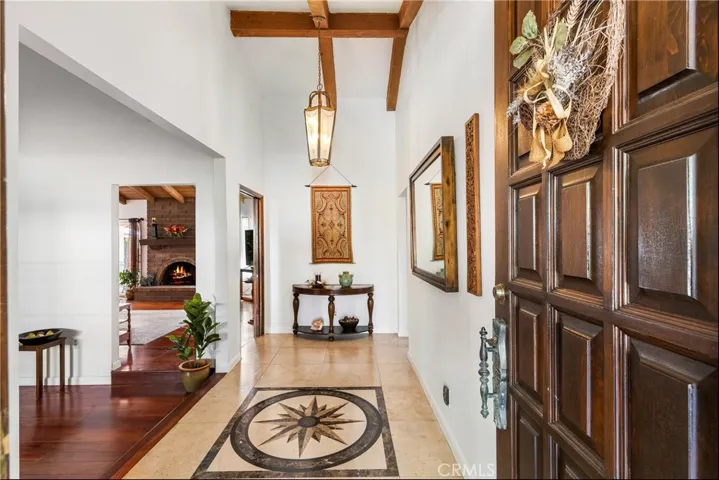 Beautiful high ceiling foyer entry with beamed ceiling and travertine floors with custom medallion inlaid display.