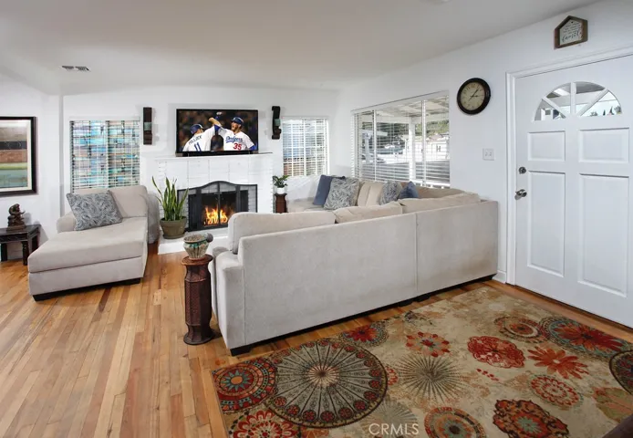 A classic white paneled front door with fanned glass insert sweeps open to a bright and flowing open concept floor plan. The living room offers an abundance of natural light from a multitude of windows and is enhanced by a raised hearth fireplace with mantle and complementary hardwood floors.