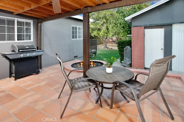 The private  backyard will be a favorite entertainment destination with its large covered patio with ceiling fan and terra cotta tile, colorful planters, fire pit, manicured hedges and towering shade/fruit trees.