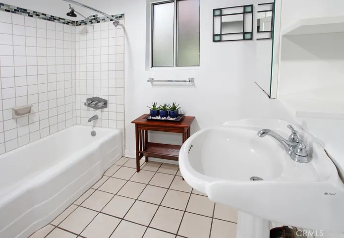 Full guest bathroom offers a pedestal sink, custom tiled tub/shower, privacy window and tiled floors