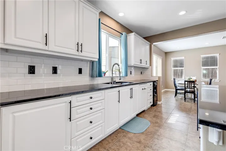 Black farmhouse sink, dishwasher has custom cabinetry and there is a trash compactor.