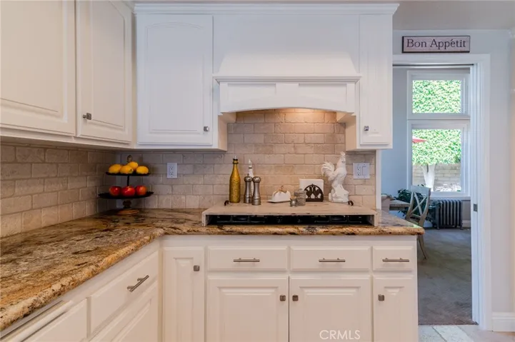 Kitchen with travertine backsplash and 5-burner stove with hood.