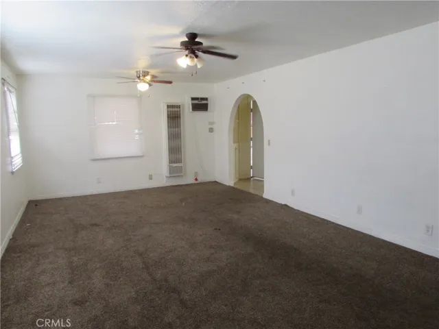 Living room has carpet, two ceiling fans, wall heater and arched entryway to the kitchen and hallway