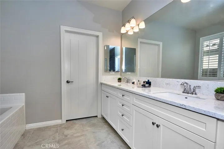 Romantic Master Bath features gorgeous quartz countertops, two sinks & large walk in closet with a gorgeous panel door, soaking tub with window and plantation shutters, and a glass enclosed shower.