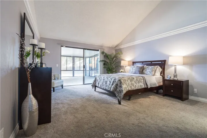 Staged master bedroom with sliding door access to the sunroom, crown molding, and wide baseboards.