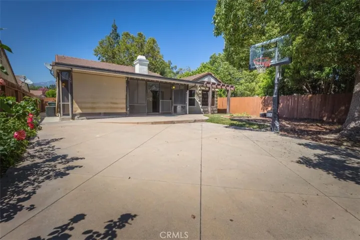 Spacious backyard hardscape with basketball hoop and gorgeous shade tree.
