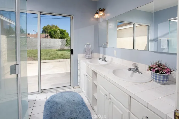 En suite master bathroom modern white vanity with abundant storage, large dressing mirror, glass enclosed step-in shower, tiled floors and private access to the backyard through the sliding glass doors.