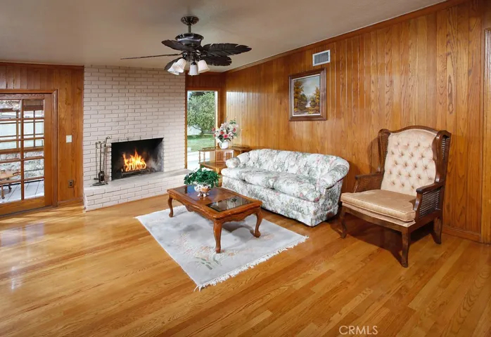 The living room is bathed in natural light from a multitude of windows and is enhanced by a designer lighted ceiling fan, floor-to-ceiling white brick fireplace, gleaming oak hardwood floors and sliding French doors that lead to the family room.