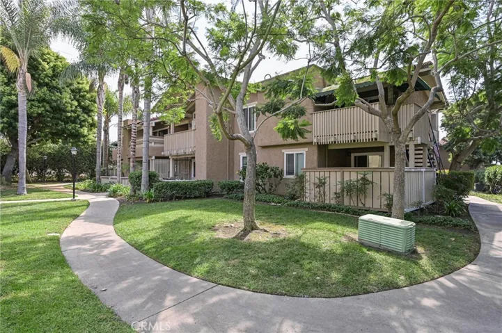 Walkway outside unit featuring grassy areas and mature trees
