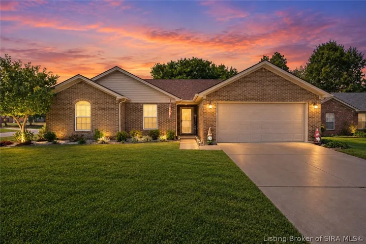 Beautiful twilight view of 6016 Pine View Ct showcasing the home’s classic brick exterior, welcoming front entry, two-car garage, and attractive landscaping. Warm exterior lighting creates inviting curb appeal against a vibrant evening sky.