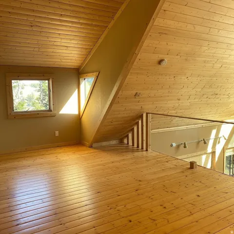 Loft space featuring wood plank flooring, wood-paneled ceilings, and multiple windows  This is the primary bedroom. Photo altered to remove a bed.