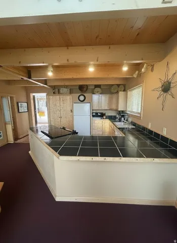 U-shaped kitchen counter with black tile surface, wood-finish cabinetry, and exposed wood ceiling beams