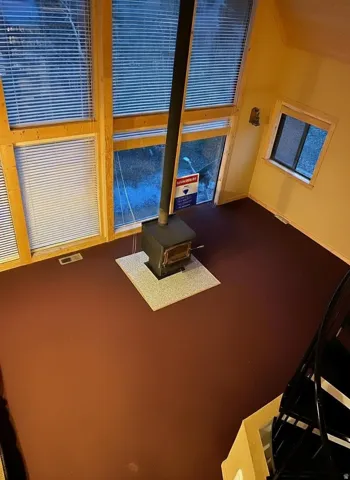 Open-concept room featuring floor-to-ceiling windows, a freestanding wood-burning stove with a hearth, and a spiral staircase