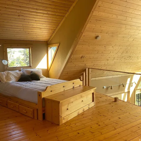 Vaulted wood-paneled ceiling, wood-plank flooring, built-in bed frame with integrated storage, and an angular window