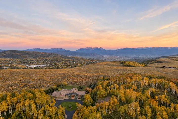 Expansive property featuring a large residence, surrounding deciduous trees, a paved driveway, and distant mountains