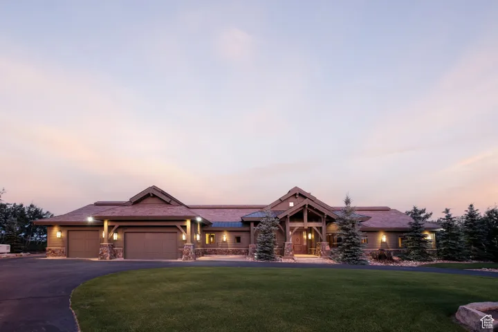 View of front of property featuring a lawn, driveway, stone siding, and a garage