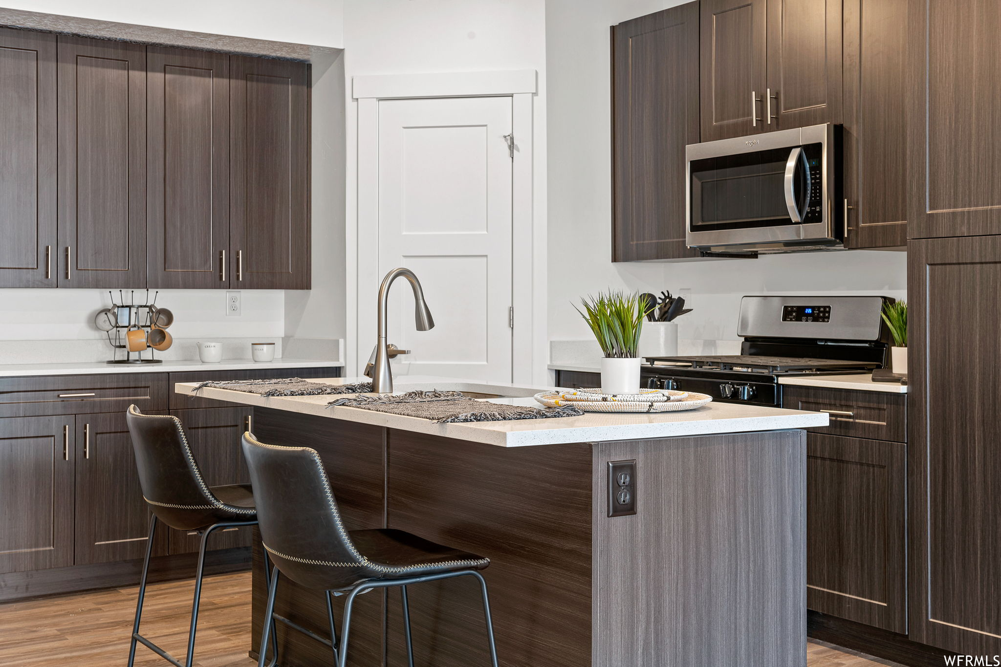 Kitchen with light countertops, a kitchen island, light hardwood floors, appliances with stainless steel finishes, and dark brown cabinetry