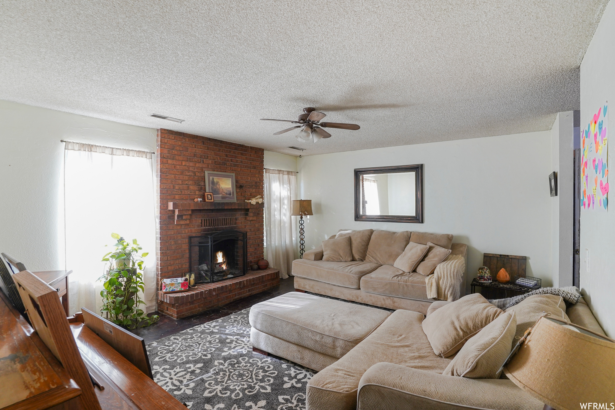 Living room featuring a fireplace, ceiling fan, plenty of natural light, and a textured ceiling