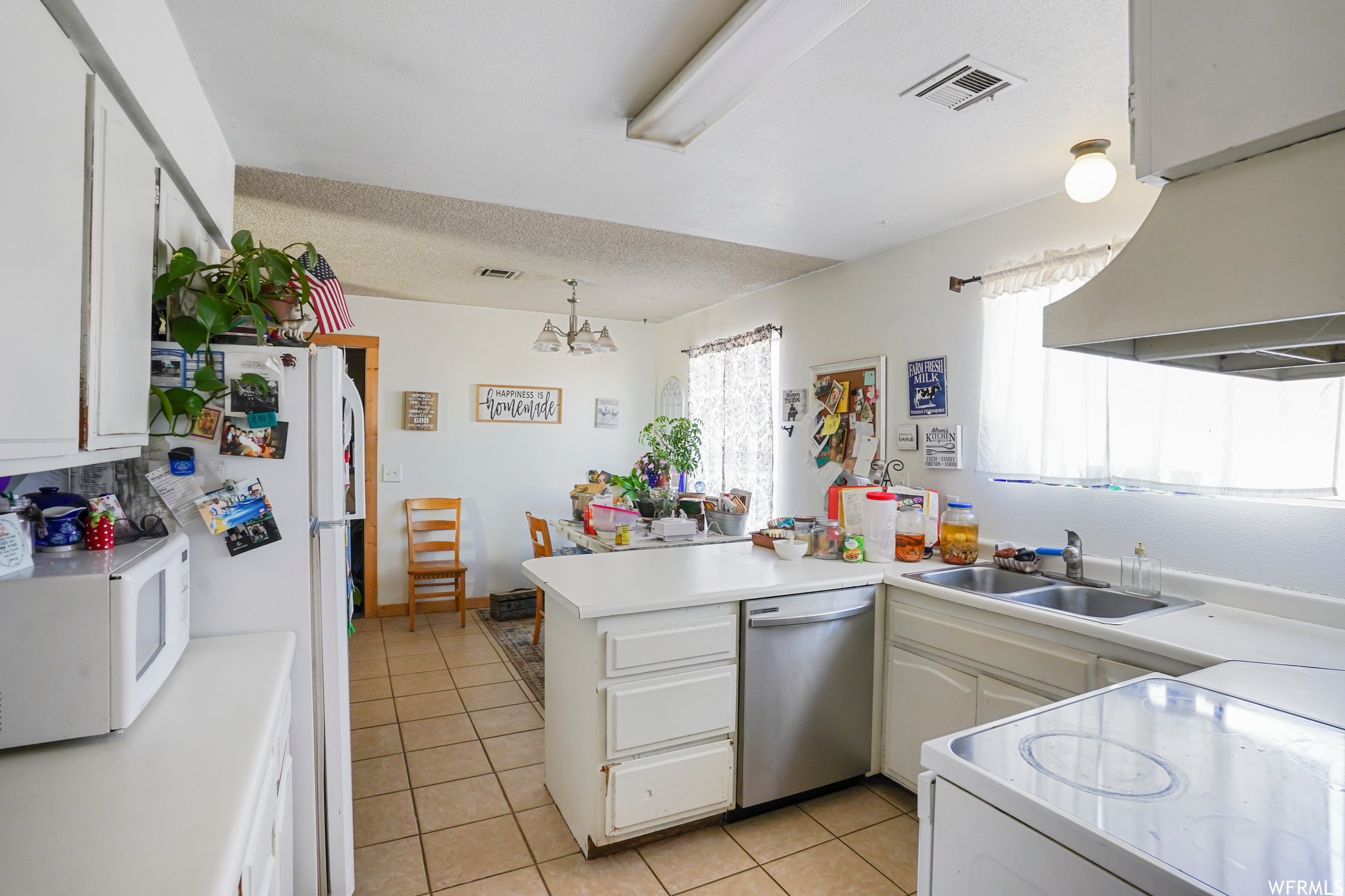 Kitchen with an inviting chandelier, dishwasher, sink, light tile floors, and kitchen peninsula