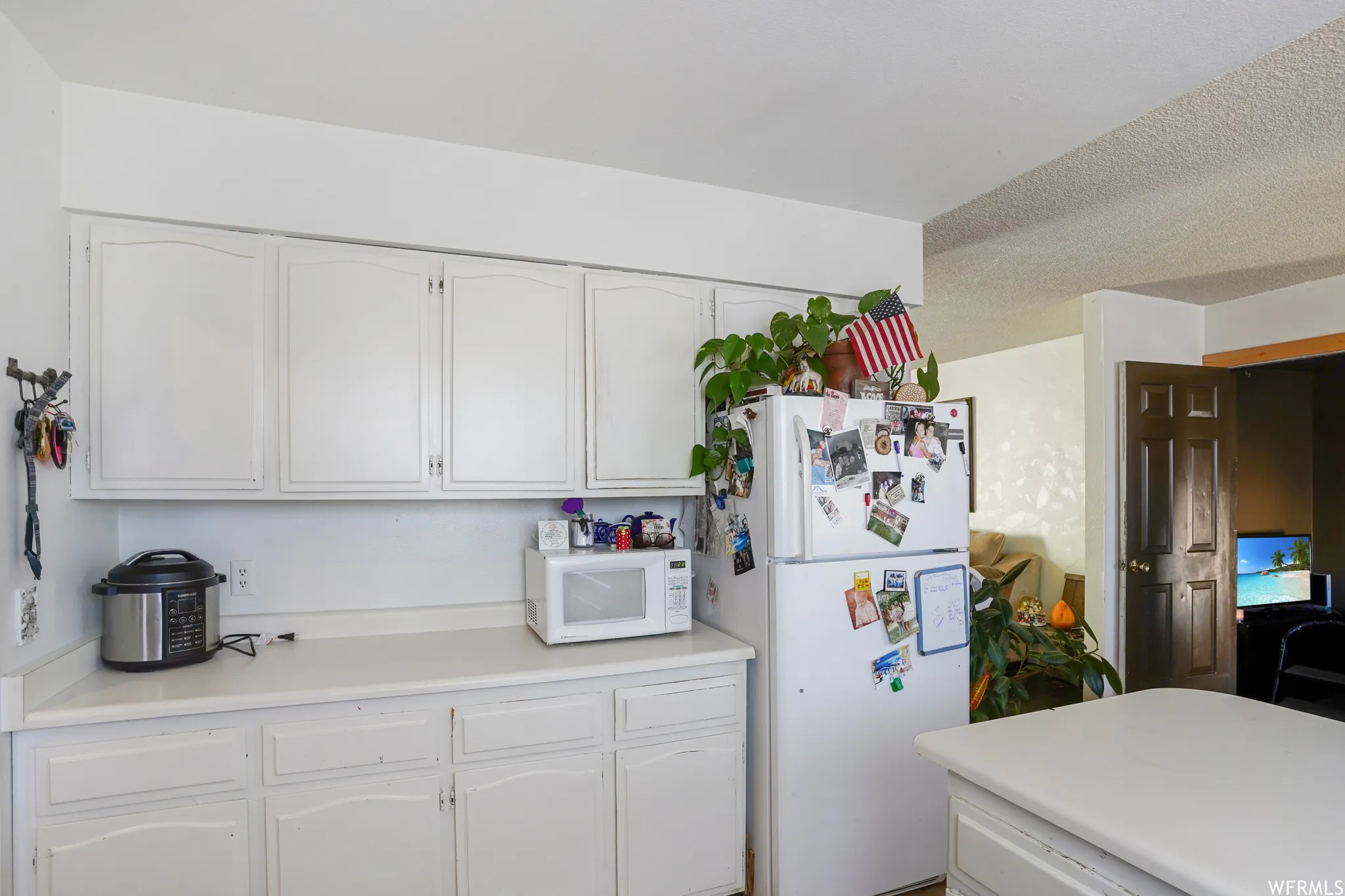 Kitchen with white appliances, a textured ceiling, and white cabinetry
