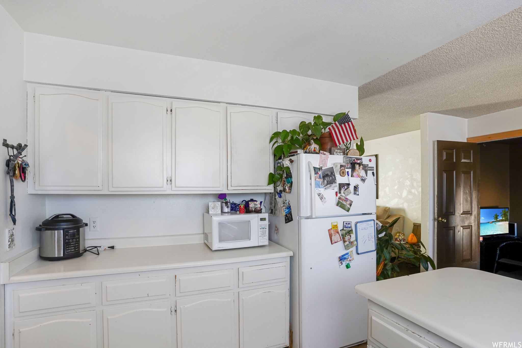 Kitchen with white appliances, a textured ceiling, and white cabinetry