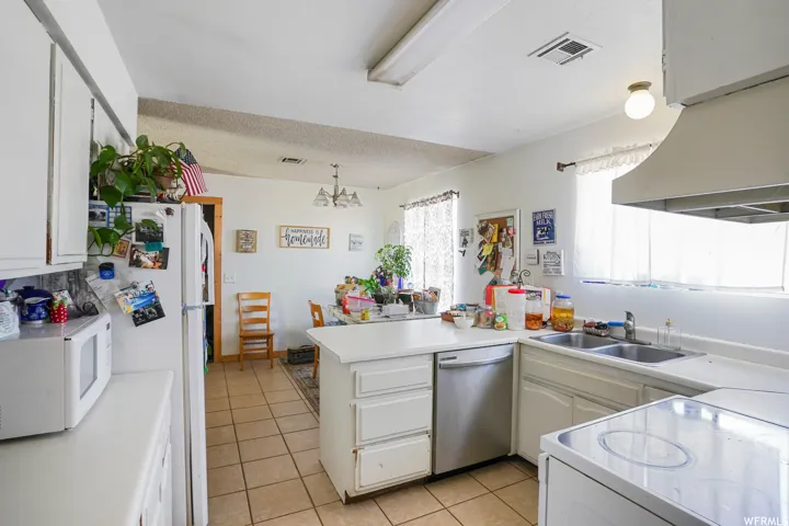 Kitchen with an inviting chandelier, dishwasher, sink, light tile floors, and kitchen peninsula