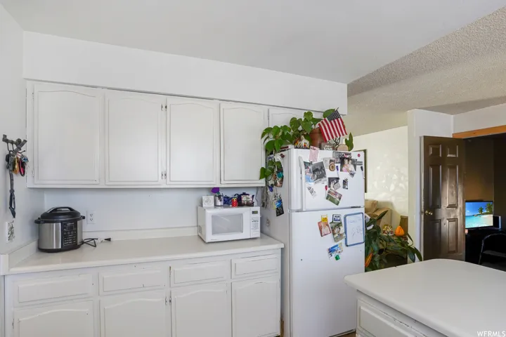 Kitchen with white appliances, a textured ceiling, and white cabinetry