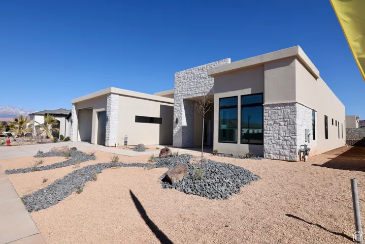 Rear view of house with a garage, stone siding, driveway, and stucco siding