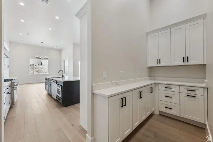 Kitchen with a sink, light countertops, a notable chandelier, recessed lighting, and light wood-style flooring