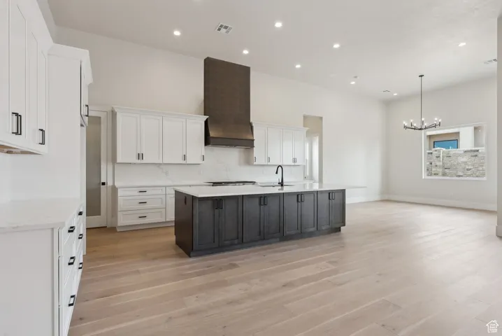 Kitchen with white cabinets, light wood finished floors, a chandelier, and premium range hood