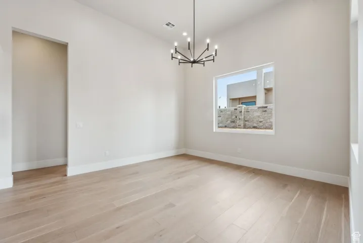 Unfurnished room with baseboards, visible vents, light wood-style flooring, and a chandelier