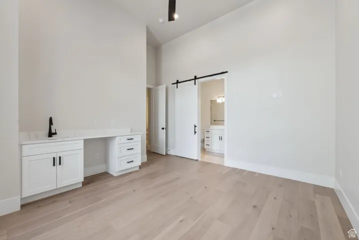 Unfurnished bedroom with a towering ceiling, a barn door, a sink, light wood finished floors, and ensuite bathroom