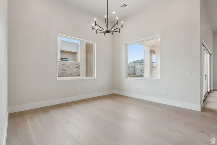 Empty room with baseboards, a notable chandelier, light wood-style flooring, and visible vents