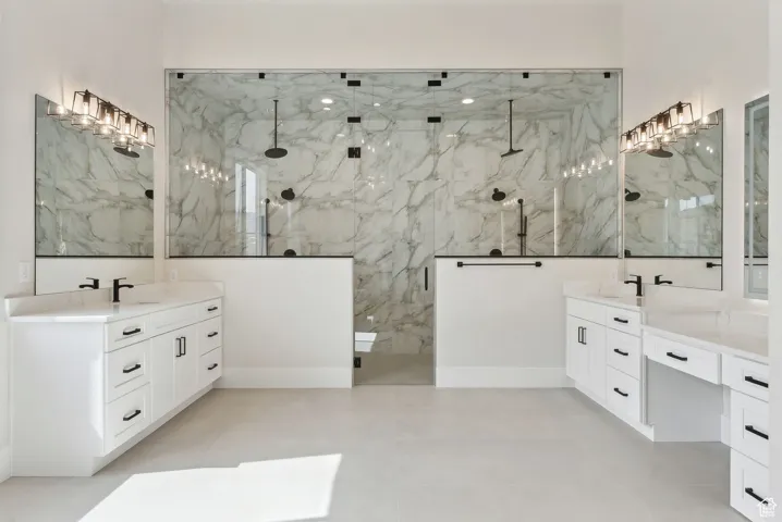 Full bath featuring a sink, a marble finish shower, and two vanities