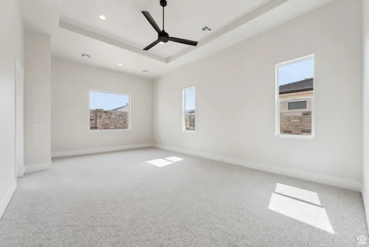 Empty room featuring a raised ceiling, carpet floors, a ceiling fan, recessed lighting, and visible vents
