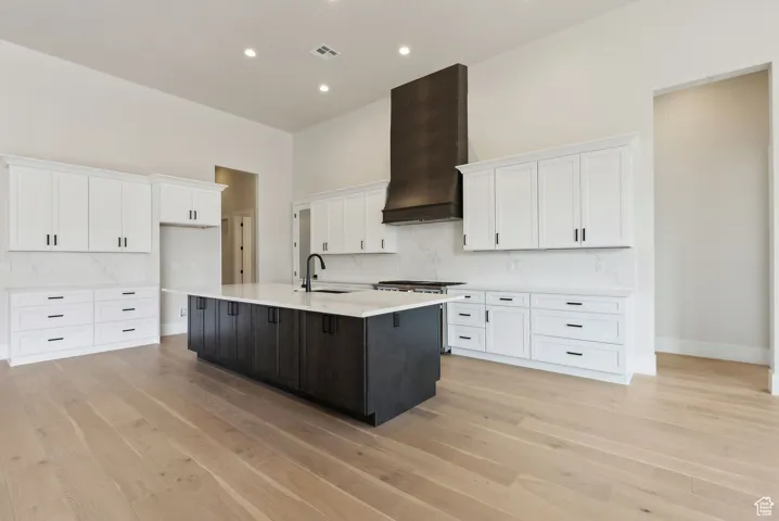 Kitchen featuring white cabinets, custom exhaust hood, a kitchen island with sink, and light countertops