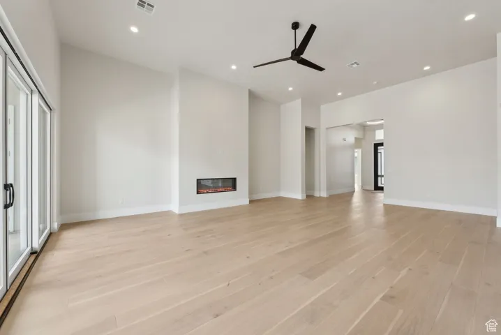 Unfurnished living room featuring a ceiling fan, visible vents, light wood-type flooring, a glass covered fireplace, and recessed lighting