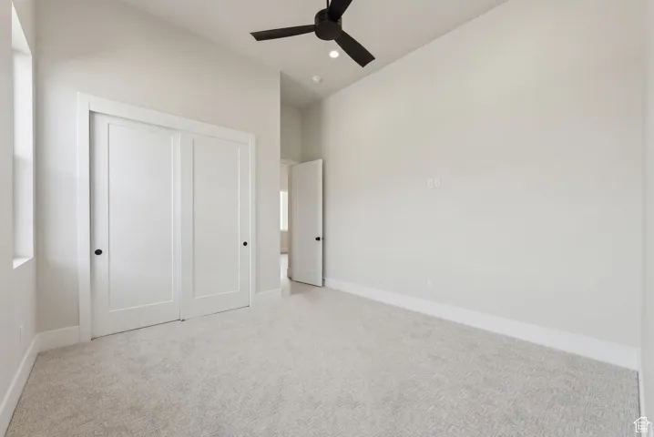 Unfurnished bedroom featuring a closet, baseboards, ceiling fan, light colored carpet, and vaulted ceiling