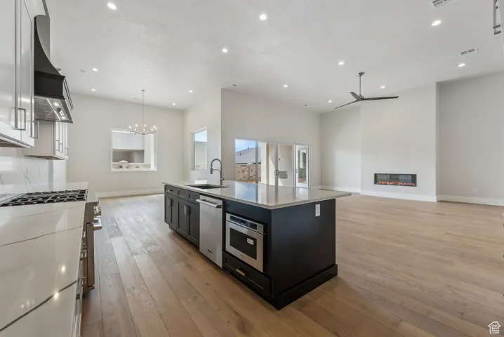 Kitchen with a sink, light countertops, light wood finished floors, ceiling fan with notable chandelier, and built in microwave