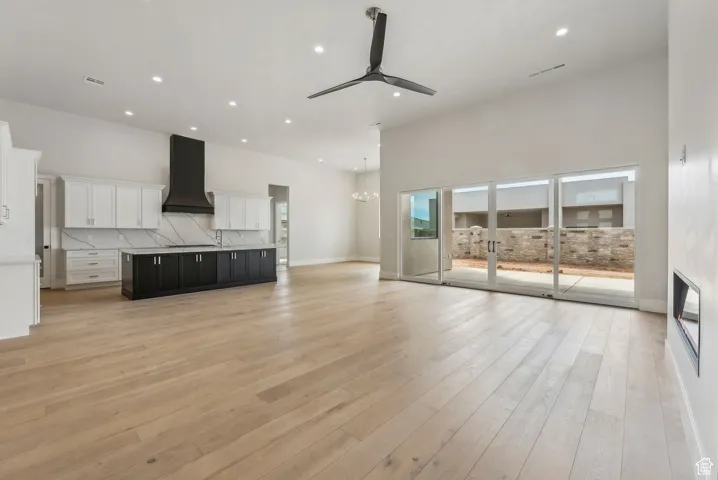 Unfurnished living room featuring recessed lighting, a towering ceiling, ceiling fan with notable chandelier, and light wood-type flooring