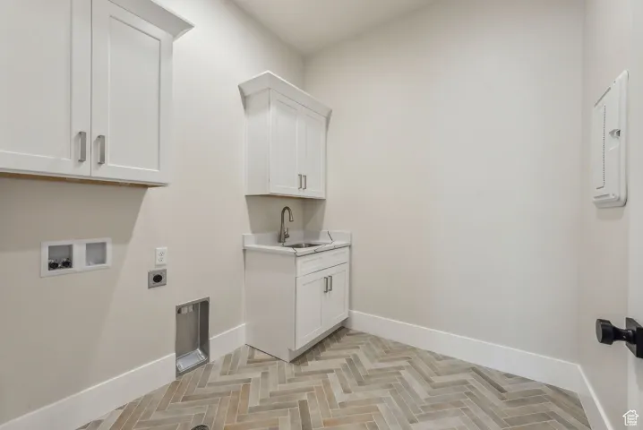 Washroom featuring electric dryer hookup, cabinet space, a sink, baseboards, and hookup for a washing machine