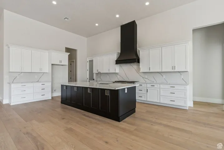 Kitchen with a sink, white cabinetry, an island with sink, and exhaust hood