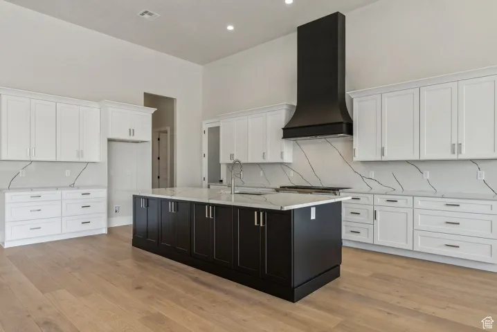Kitchen with white cabinets, custom exhaust hood, a sink, and tasteful backsplash