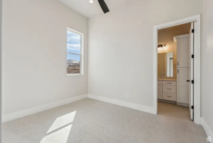 Unfurnished bedroom featuring a ceiling fan, baseboards, light carpet, and ensuite bath
